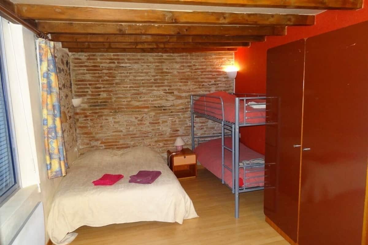 A room with a bunk bed, a wooden ceiling, a brick wall, and a wardrobe.