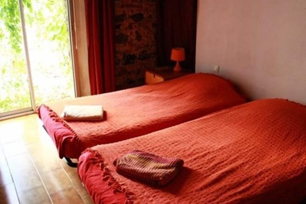 A room with two beds, a window, and a stone wall.