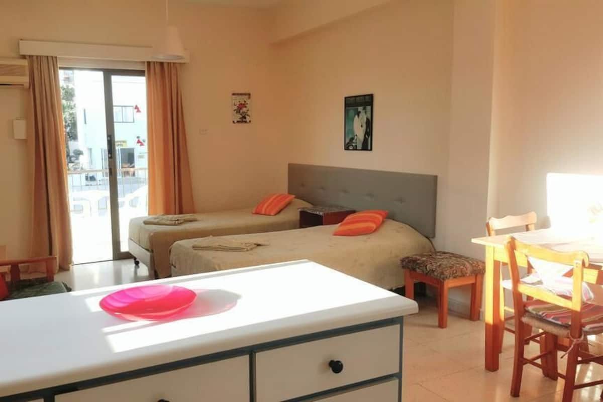 Una habitación de hotel con dos camas, una mesa de comedor y una kitchenette.