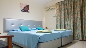 Quarto com duas camas, cabeceira, ar condicionado fixado na parede e cortina florida.