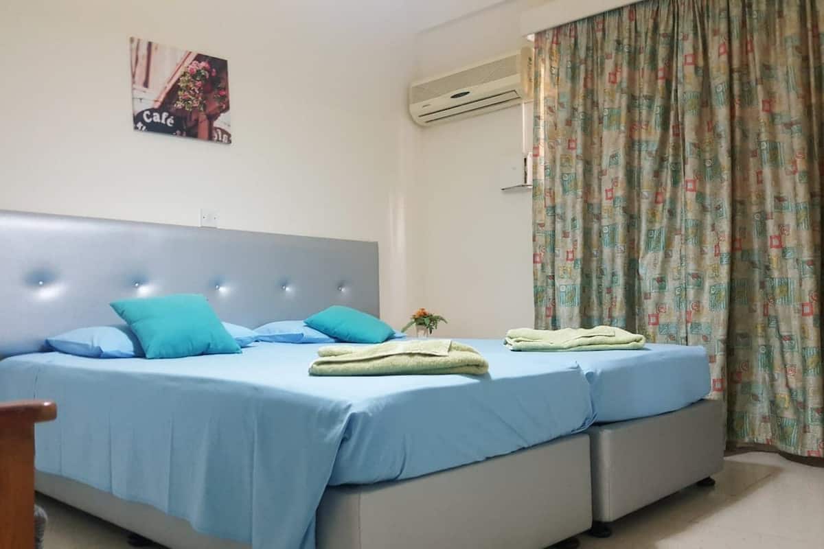 Un dormitorio con dos camas, cabeceros, aire acondicionado de pared y cortina estampada.