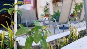 Uma área externa com mesas e cadeiras, um balcão de recepção e plantas em vasos.