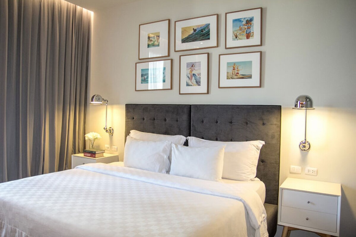 Une chambre d’hôtel avec un grand lit, deux tables de chevet, une tête de lit et six tableaux encadrés accrochés au mur.