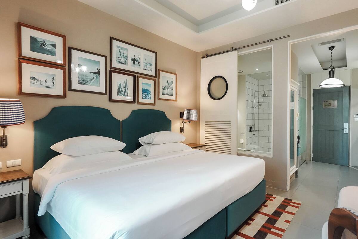 Habitación de hotel con una cama grande, un baño con ducha de vidrio y cuadros en la pared.