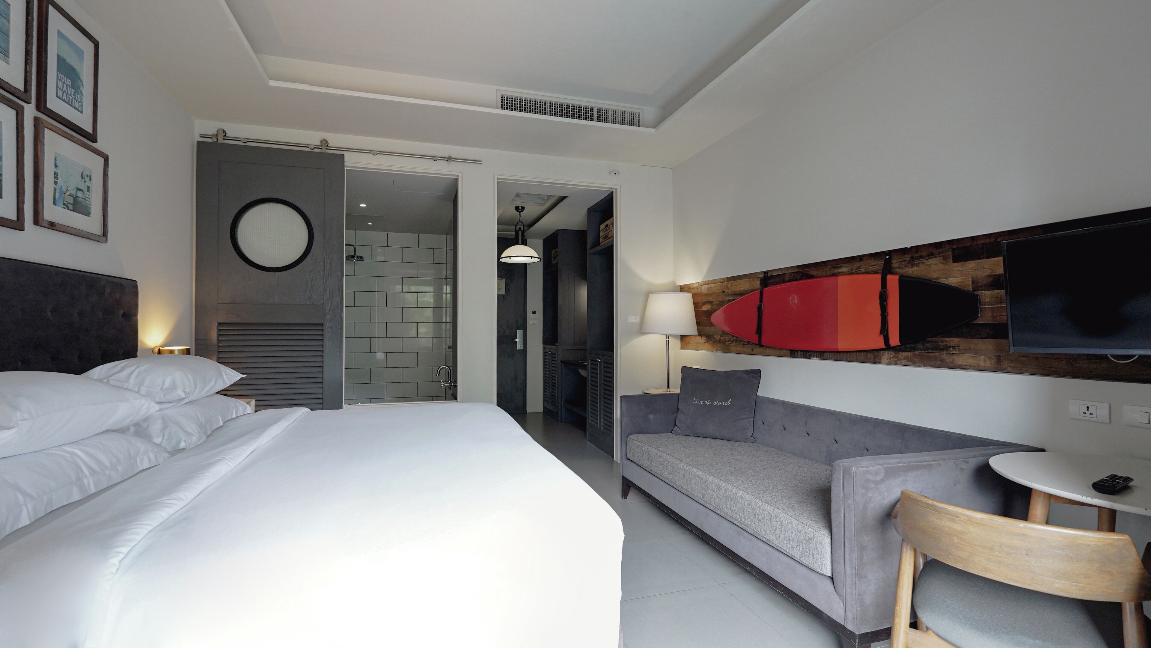 A modern hotel room with a large bed, a grey sofa, a small table, and a TV mounted on the wall.