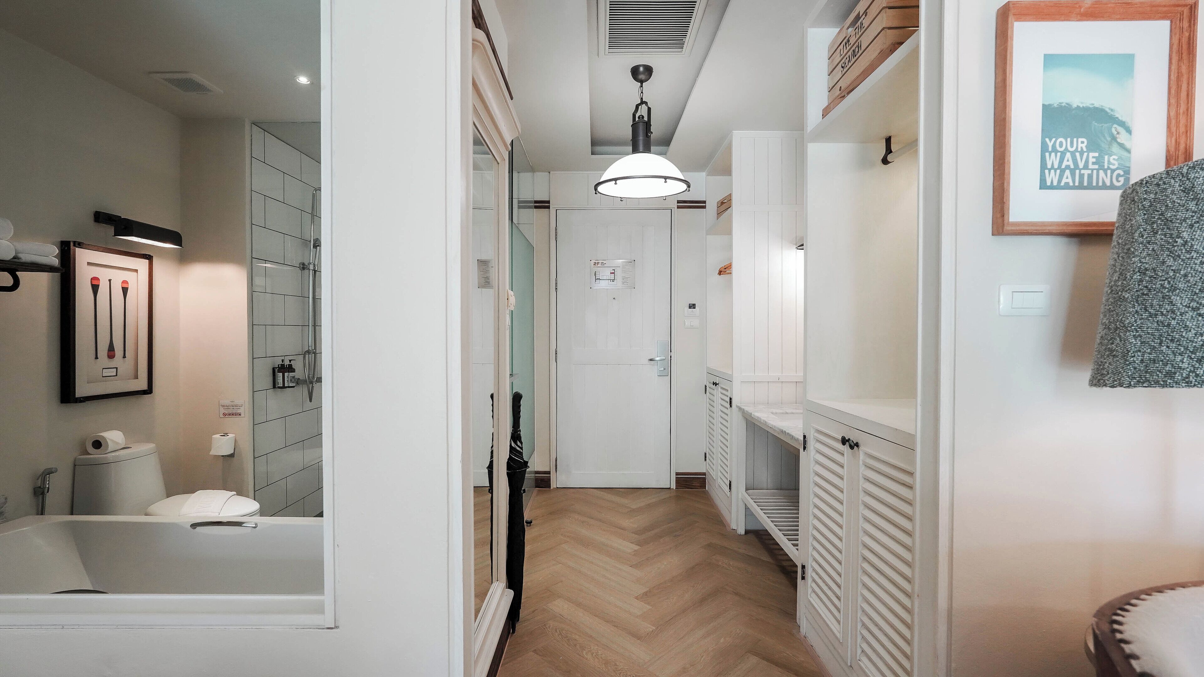 A hotel hallway with a wooden floor, a shower area, and a framed picture on the wall.
