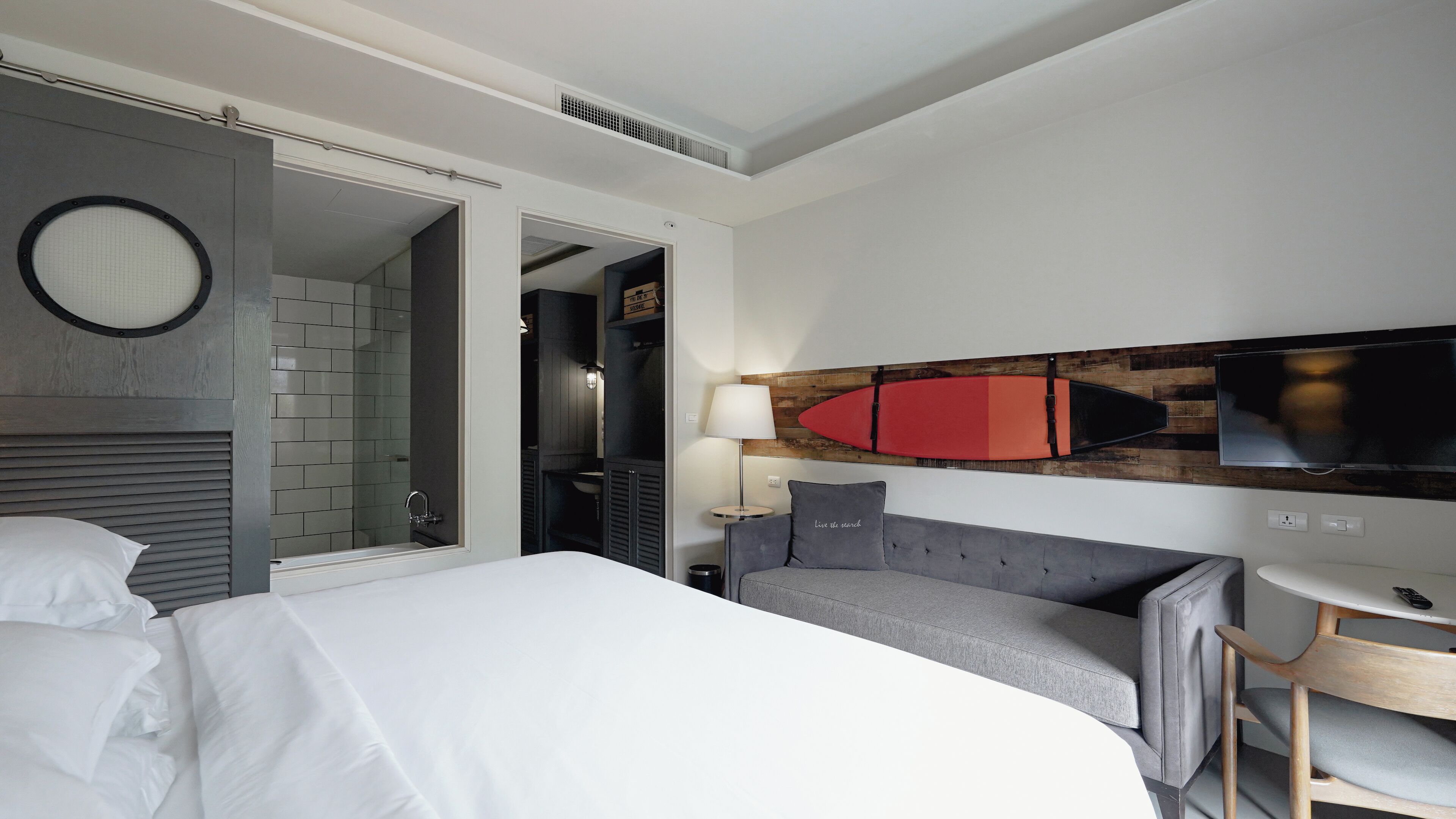 A hotel room with a bed, a desk, a chair, a TV, and a bathroom visible through an open door.