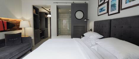 A modern hotel room with a bed, a sofa, a walk-in closet, and a bathroom.