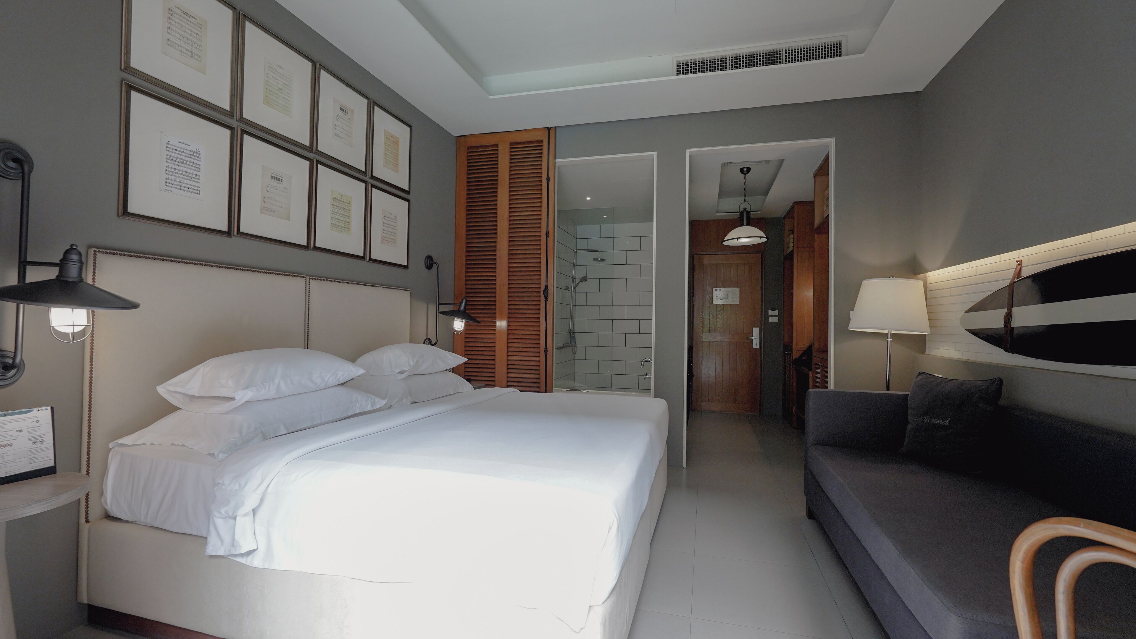 A hotel room with a bed, a sofa, a shower area, and framed certificates on the wall.