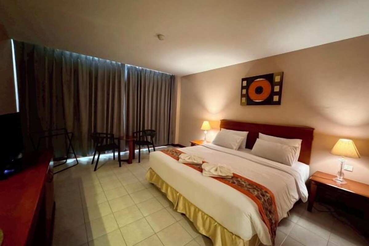 A hotel room with a large bed, two bedside lamps, a TV, a desk, and a chair.