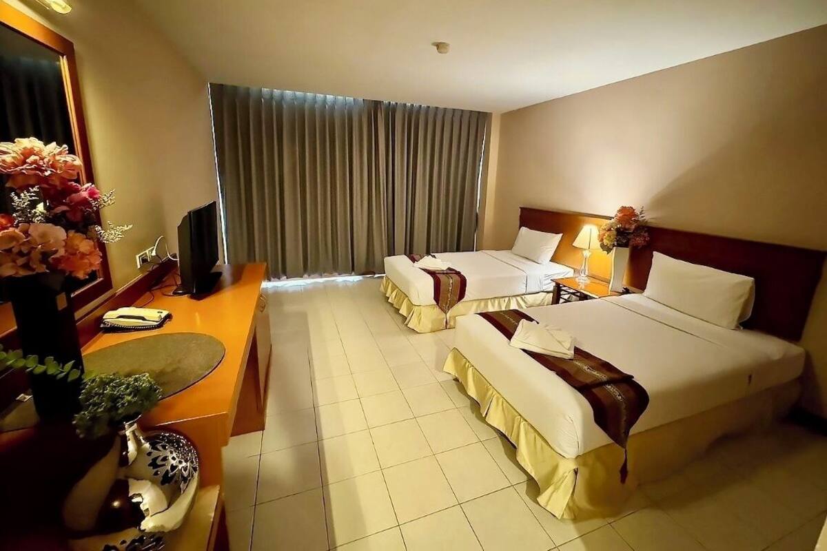 A hotel room with two beds, a desk, a chair, a TV, and a large window with curtains.