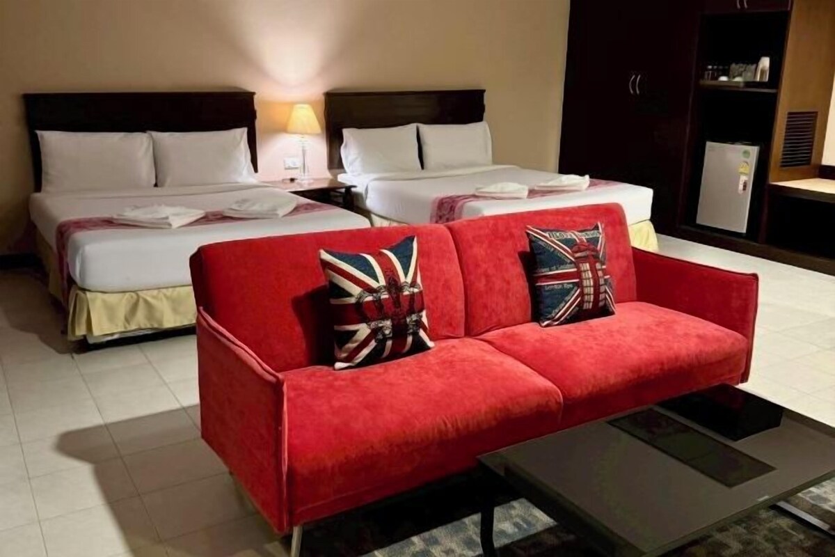 A hotel room with two beds, a red sofa, and a small table.