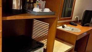 Een kleine hotelkamer met kitchenette, een koelkast, een bureau met computer en een spiegel.