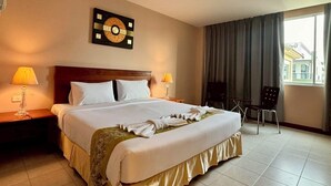 Een hotelkamer met een groot bed, twee bedlampen, een stoel, een raam met gordijnen en een wandklok.
