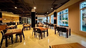 Een ruime restaurantzaal met hoge plafonds, zichtbare balken en grote ramen met uitzicht op buiten. Tafels en stoelen zijn netjes gerangschikt en de vloer is gepoetst.