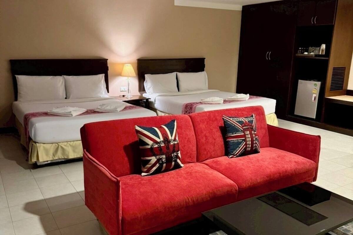 A hotel room with a red sofa, two beds, a small table, and a kitchenette.