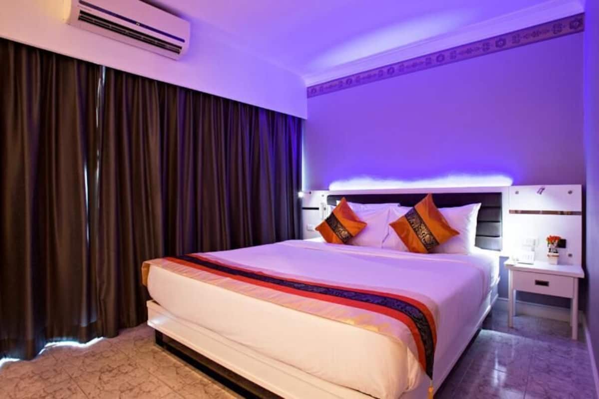 A hotel room with a large bed, a nightstand, an air conditioning unit, and a curtain.