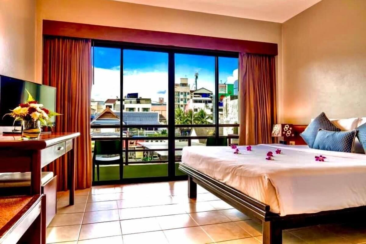 A hotel room with a bed, a desk with a TV, and a view of the city through large windows.