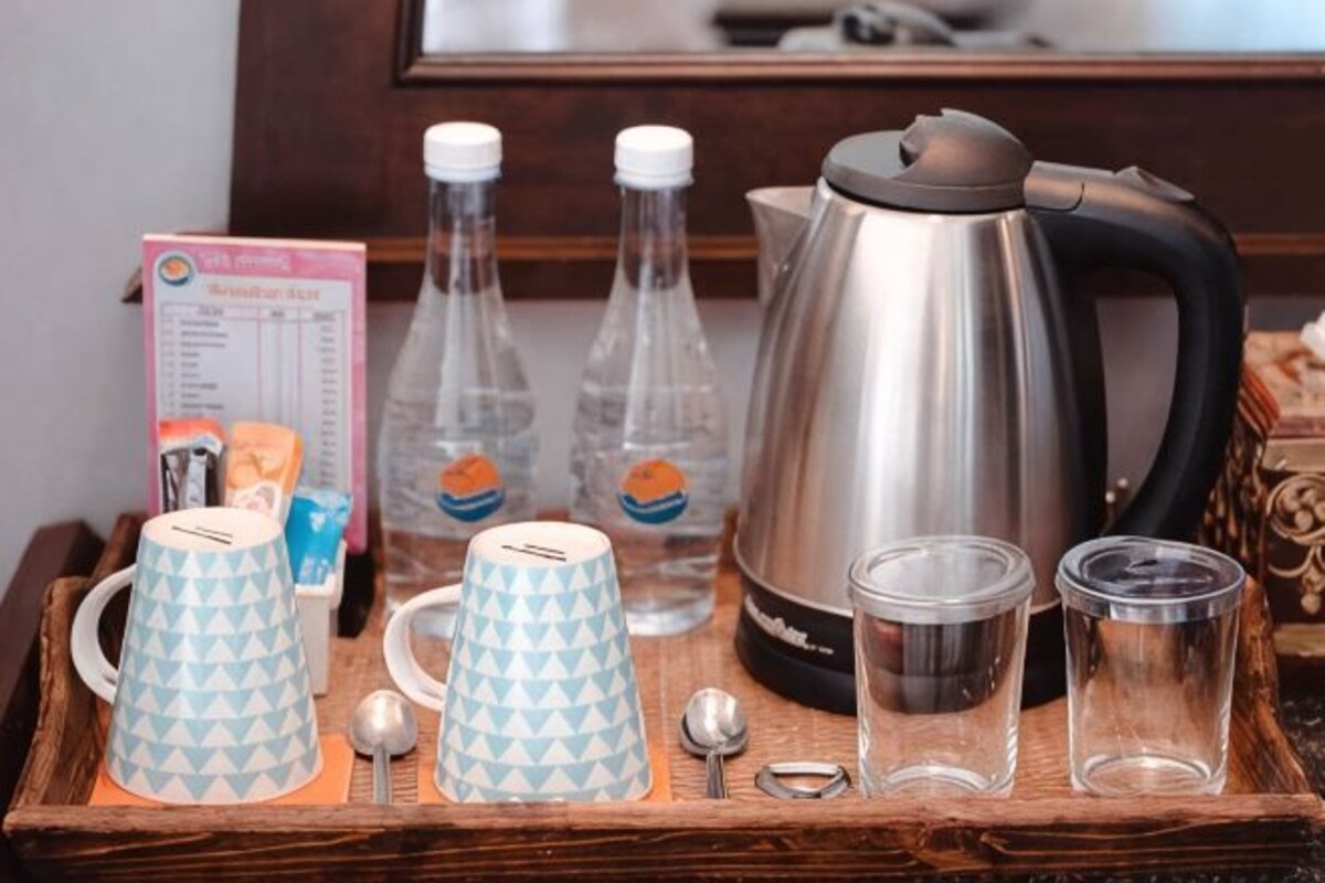 Una bandeja con un hervidor, dos botellas de agua, una cafetera, dos tazas decoradas, un menú y vasos para chupitos.