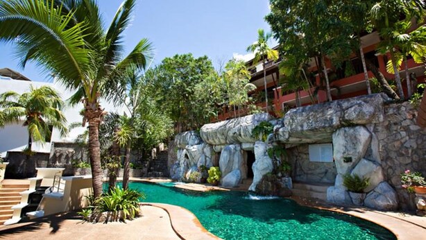 A pool area with clear water, palm trees, and a rocky wall. - C&N Resort and Spa (Patong)