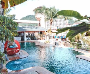 A swimming pool with a curved design, surrounded by tropical plants and palm trees. - C&N Resort and Spa (Patong)
