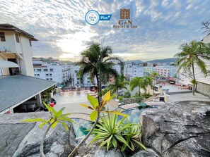 A rooftop pool area with lounge chairs and palm trees, surrounded by buildings. - C&N Resort and Spa (Patong)