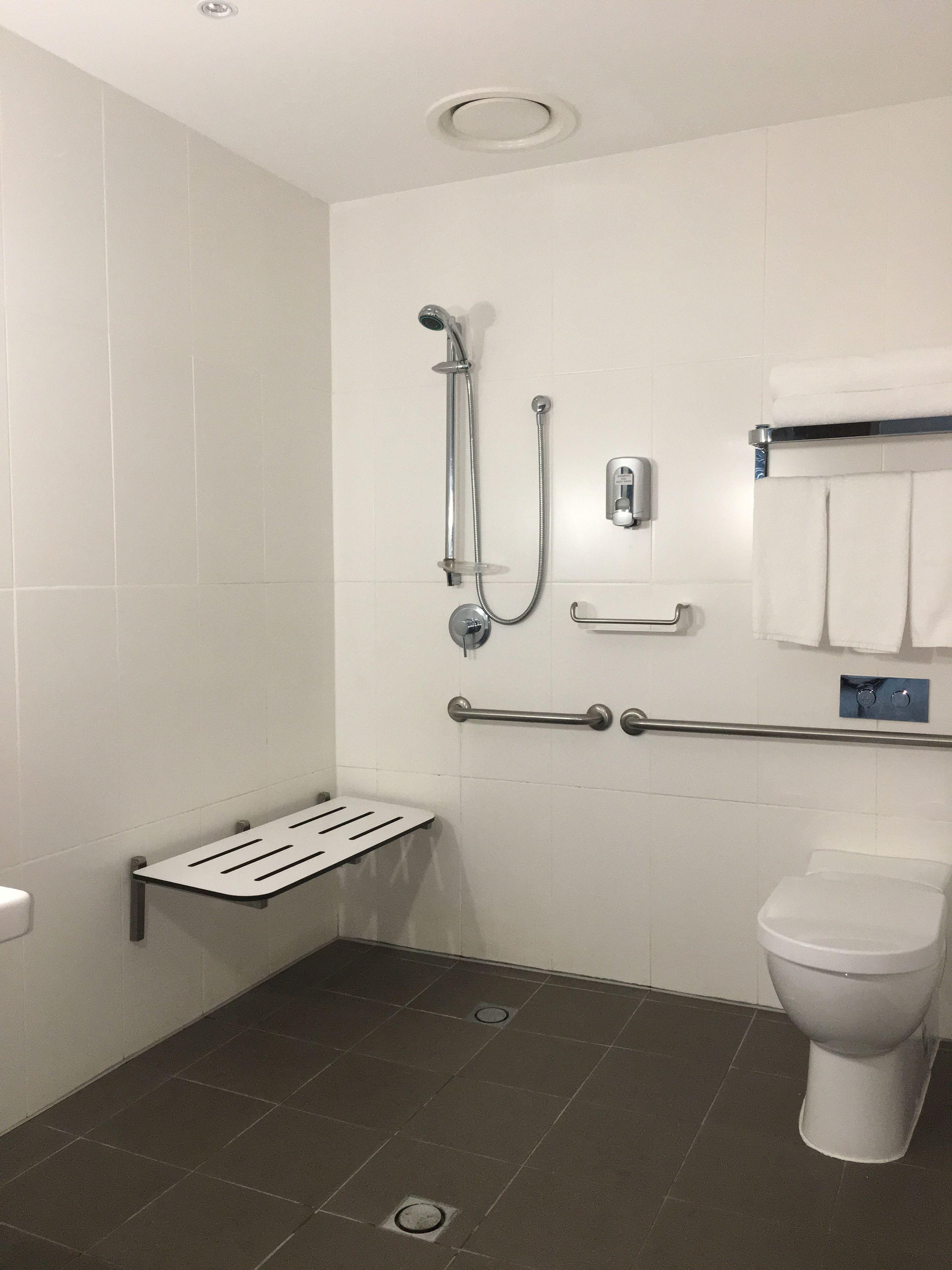A bathroom with a shower, toilet, grab bars, and a towel rack.