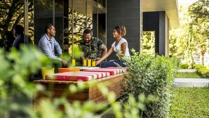 A modern outdoor seating area with wooden benches and yellow chairs, surrounded by greenery. - Holiday Inn Express Port Moresby by IHG (Port Moresby)