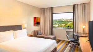 A hotel room with a large bed, a desk with a chair, a TV, and a window with a view of hills and buildings. - Holiday Inn Express Port Moresby by IHG (Port Moresby)