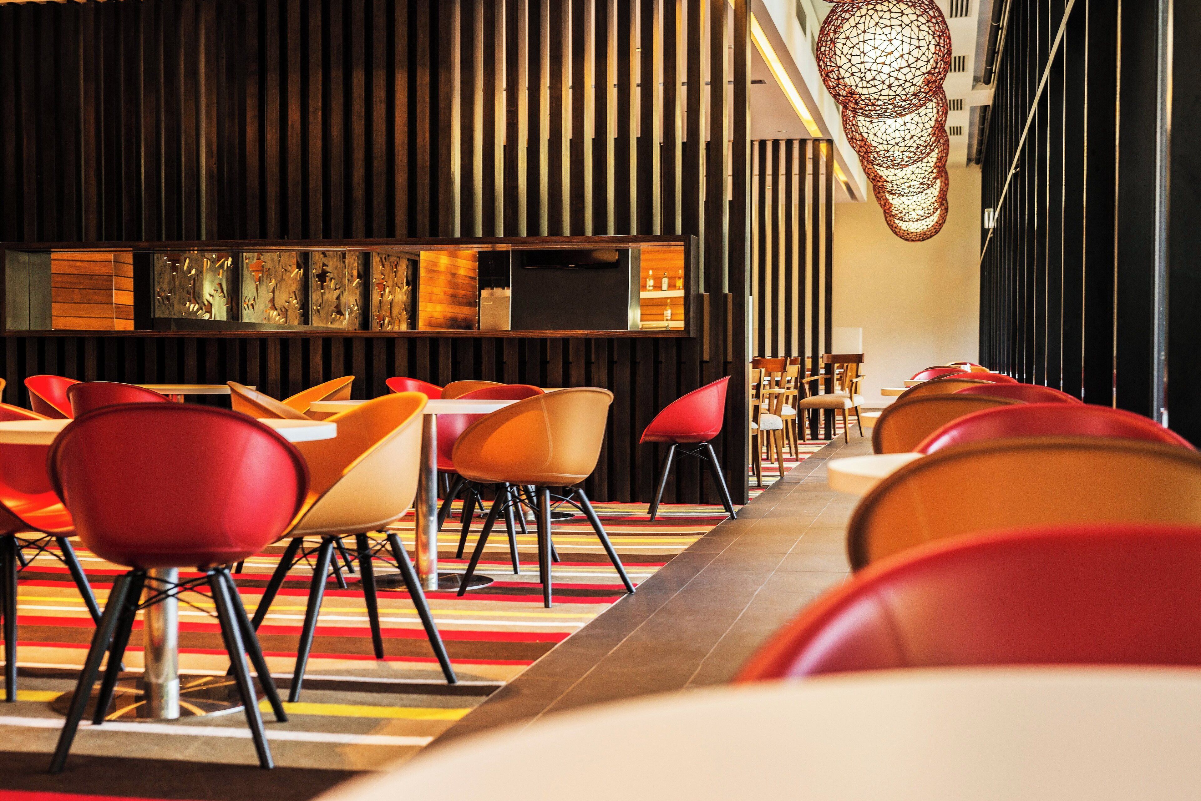 A modern restaurant interior with a long counter, red and orange chairs, and a patterned floor.