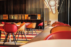 A modern restaurant interior with a long counter, red and orange chairs, and a patterned floor. - Holiday Inn Express Port Moresby by IHG (Port Moresby)