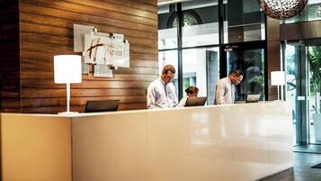 A reception desk with a wooden panel wall, a sign for Holiday Inn Express, and two individuals working at computers.