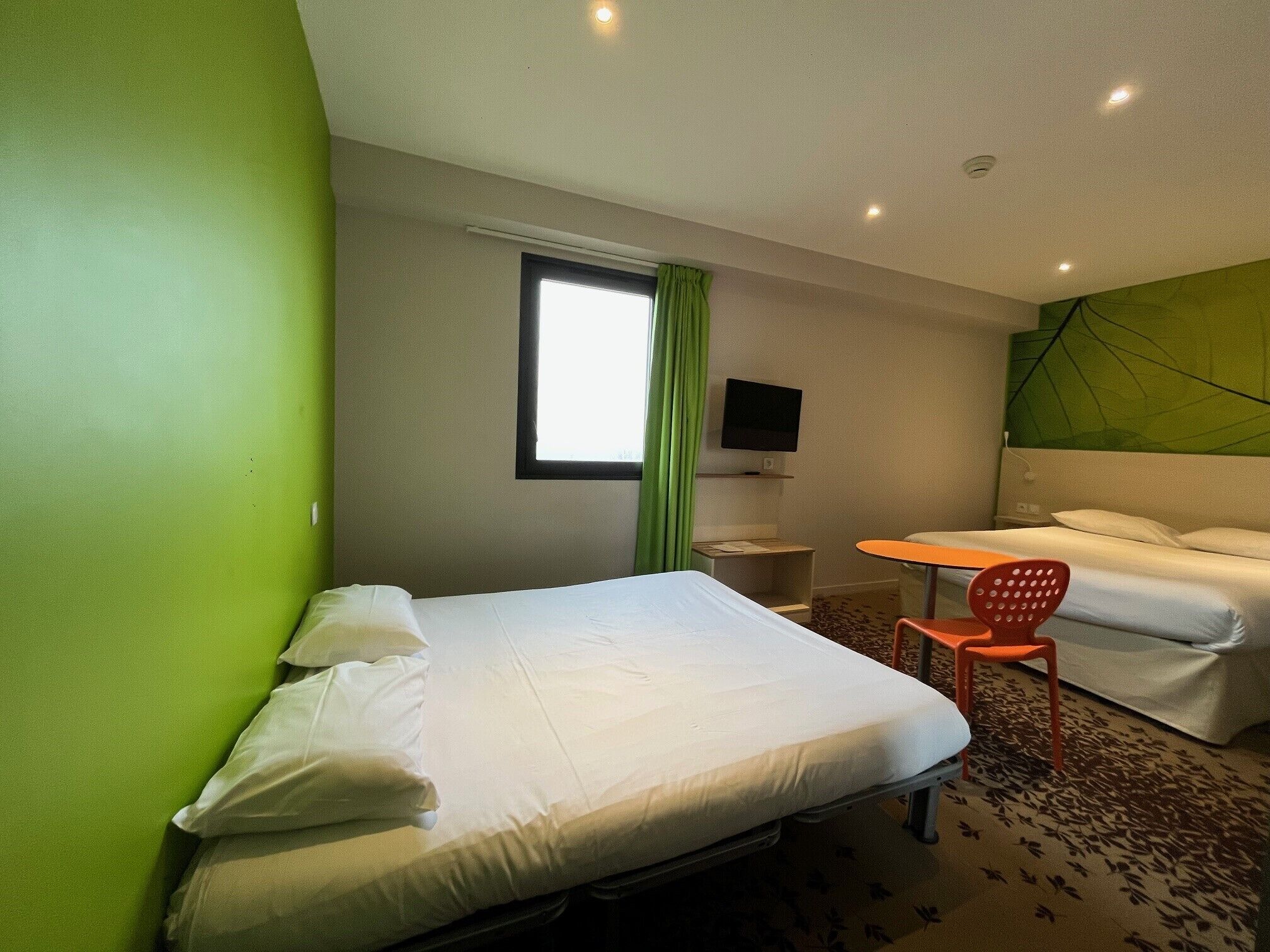 A hotel room with a bed, a small table, a TV, and a chair.