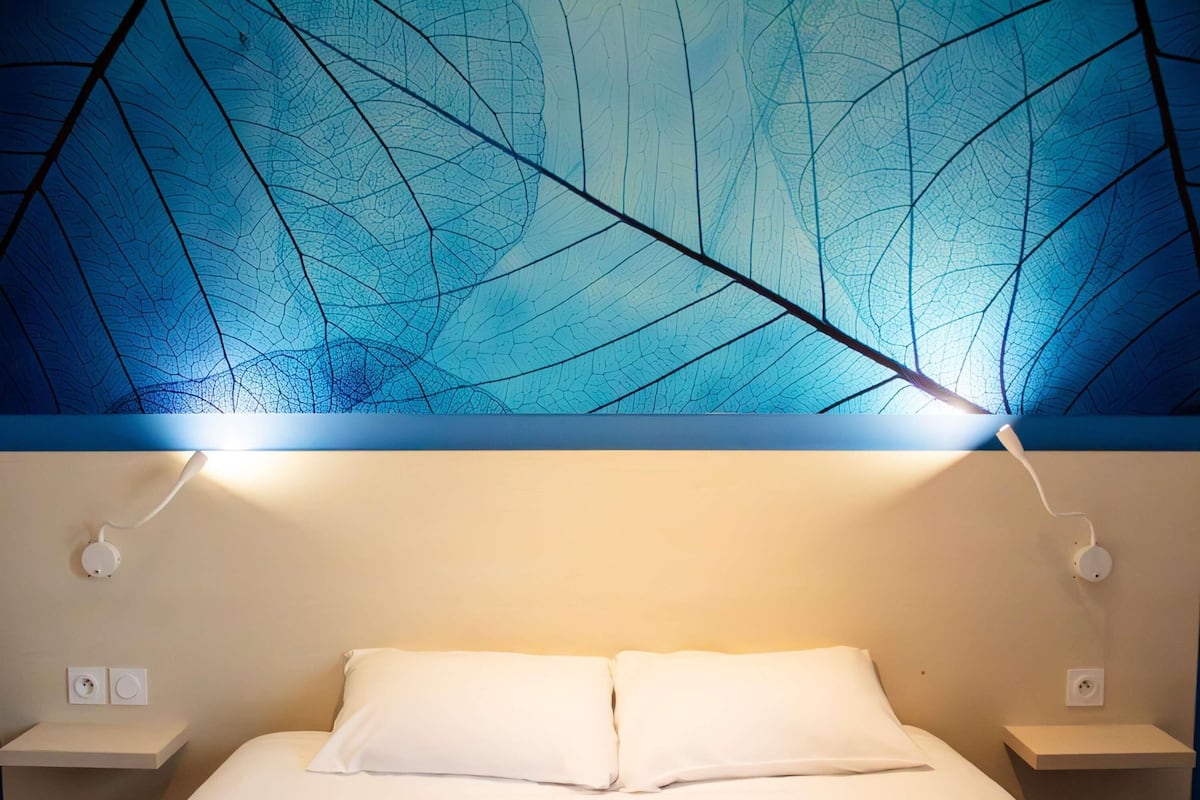 A bed with white linens, two bedside tables, and a wall with a leaf-patterned design.