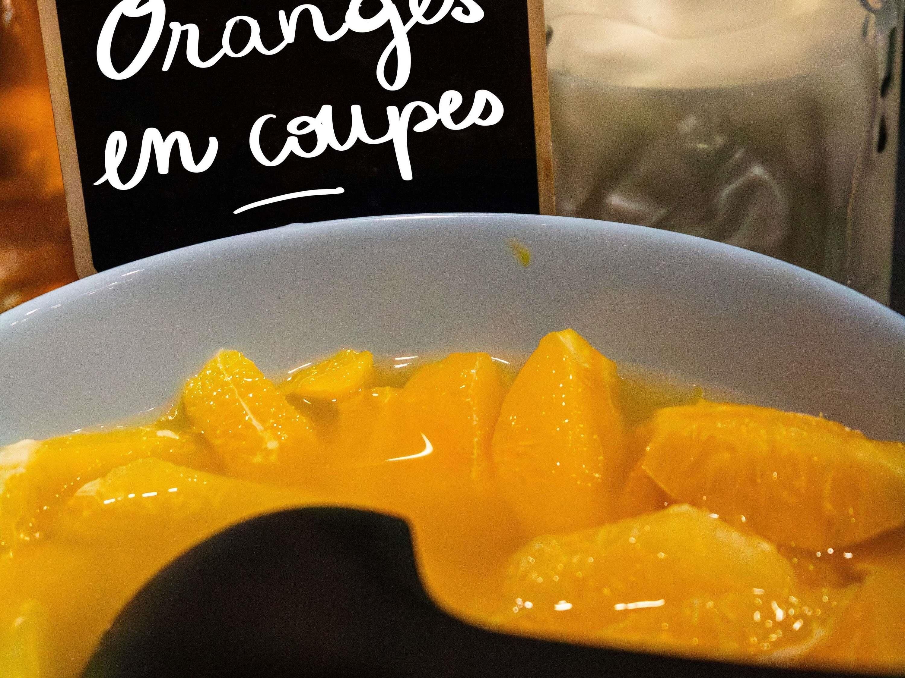 A bowl of orange slices with a sign reading 'Oranges en coupes.'