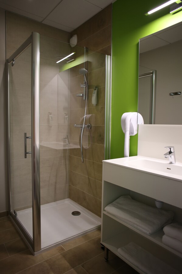 A modern bathroom with a glass-enclosed shower, a white sink, and a green accent wall.