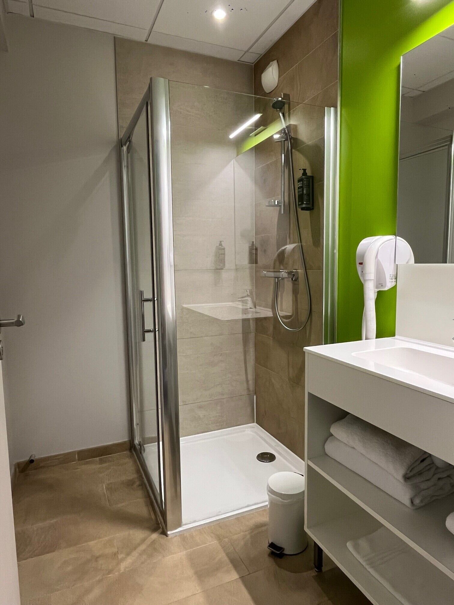 A modern bathroom with a glass-enclosed shower, a white sink, and a green accent wall.