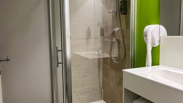 A modern bathroom with a glass-enclosed shower, a white sink, and a green accent wall.