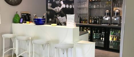 Una zona de bar con un mostrador blanco, taburetes, un reloj y un cartel de un futbolista.