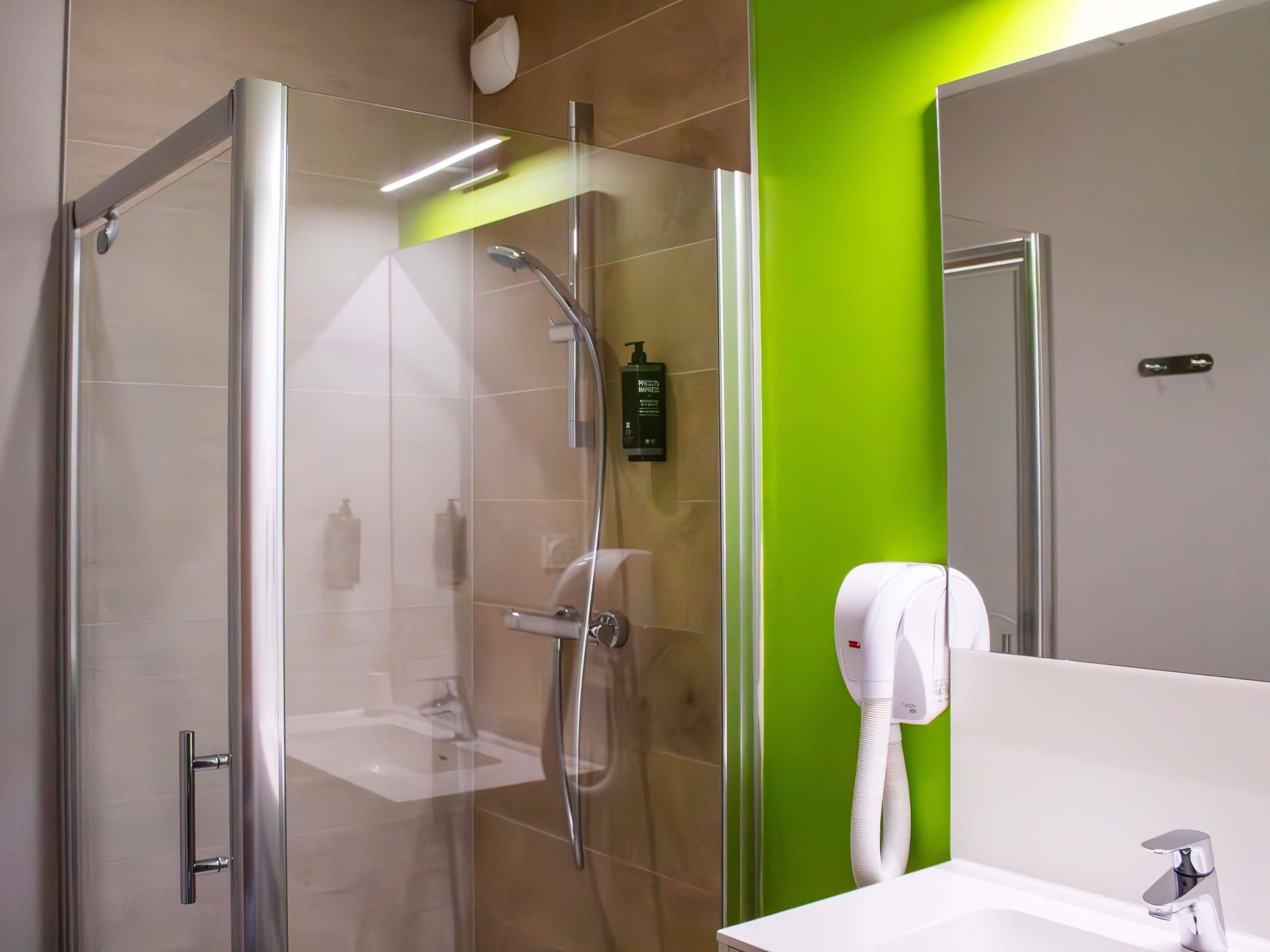 Een moderne badkamer met een douchecabine van glas, een wit wastafeltje en een groene accentmuur.