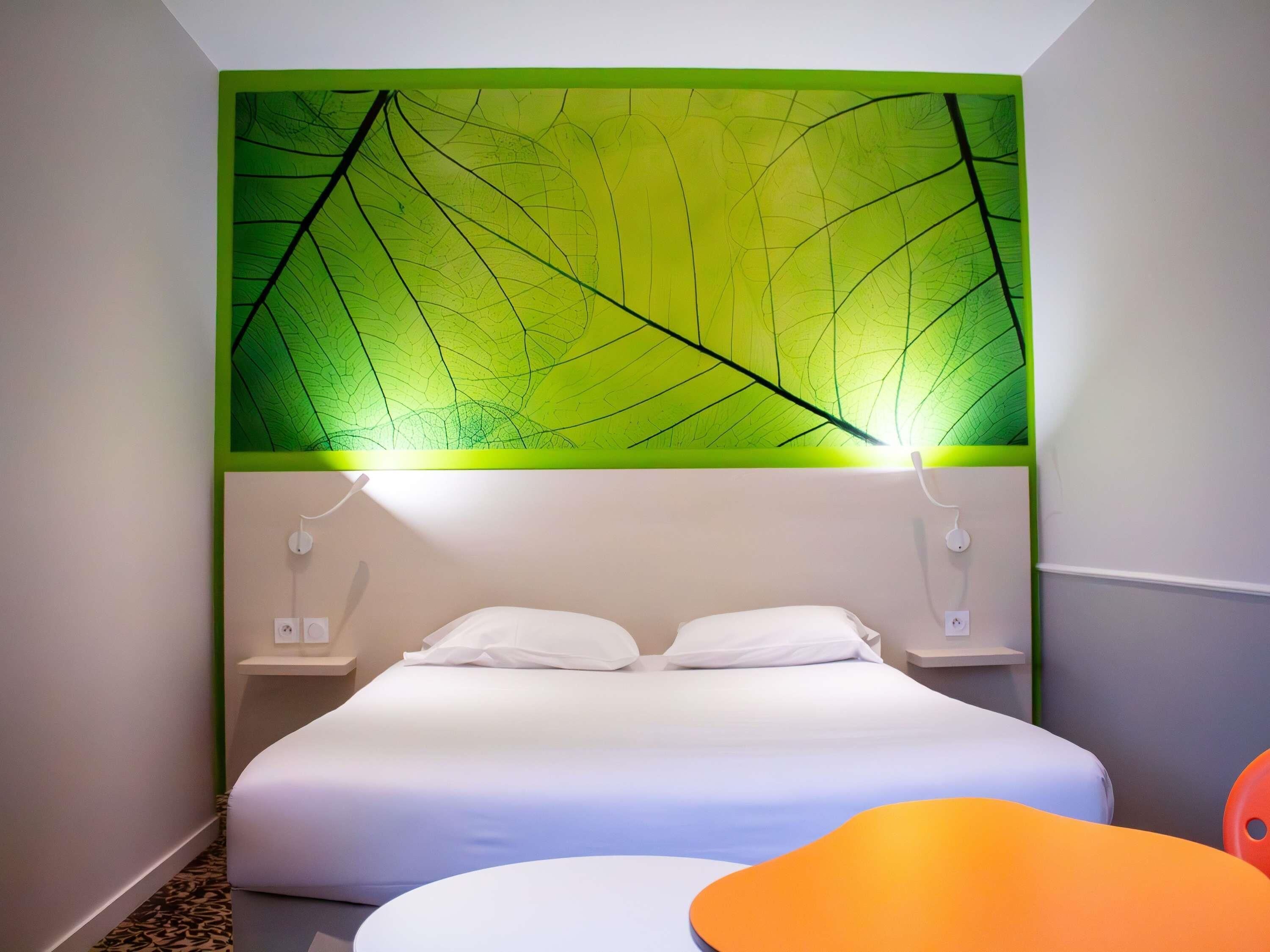 Een hotelkamer met een bed, nachtkastjes en een muur met een bladmotief.