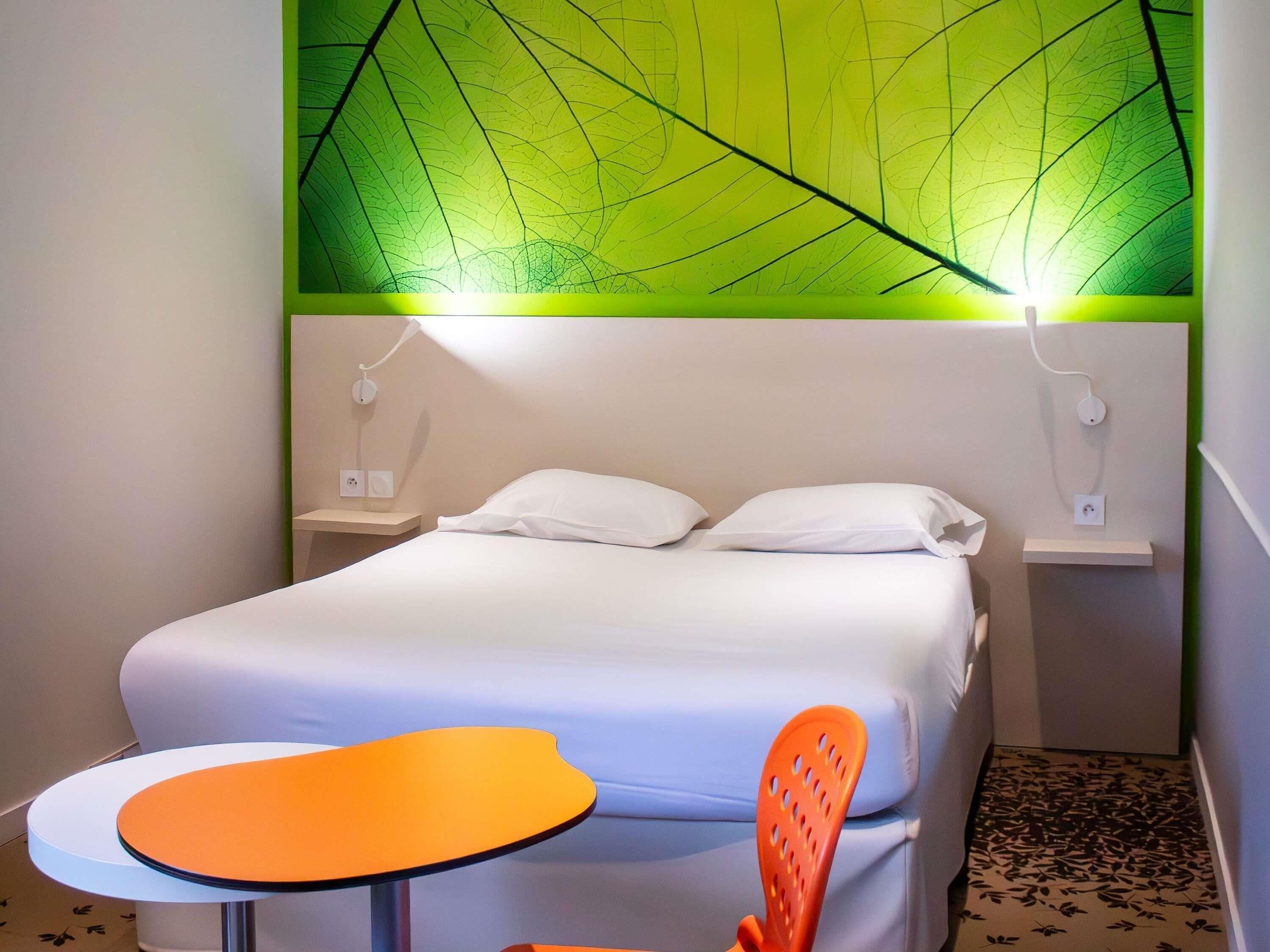 A hotel room with a bed, a nightstand, a table, and a chair.