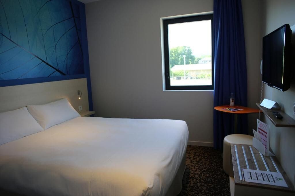 A hotel room with a large bed, a small desk, a television, and a window with a view of the outdoors.