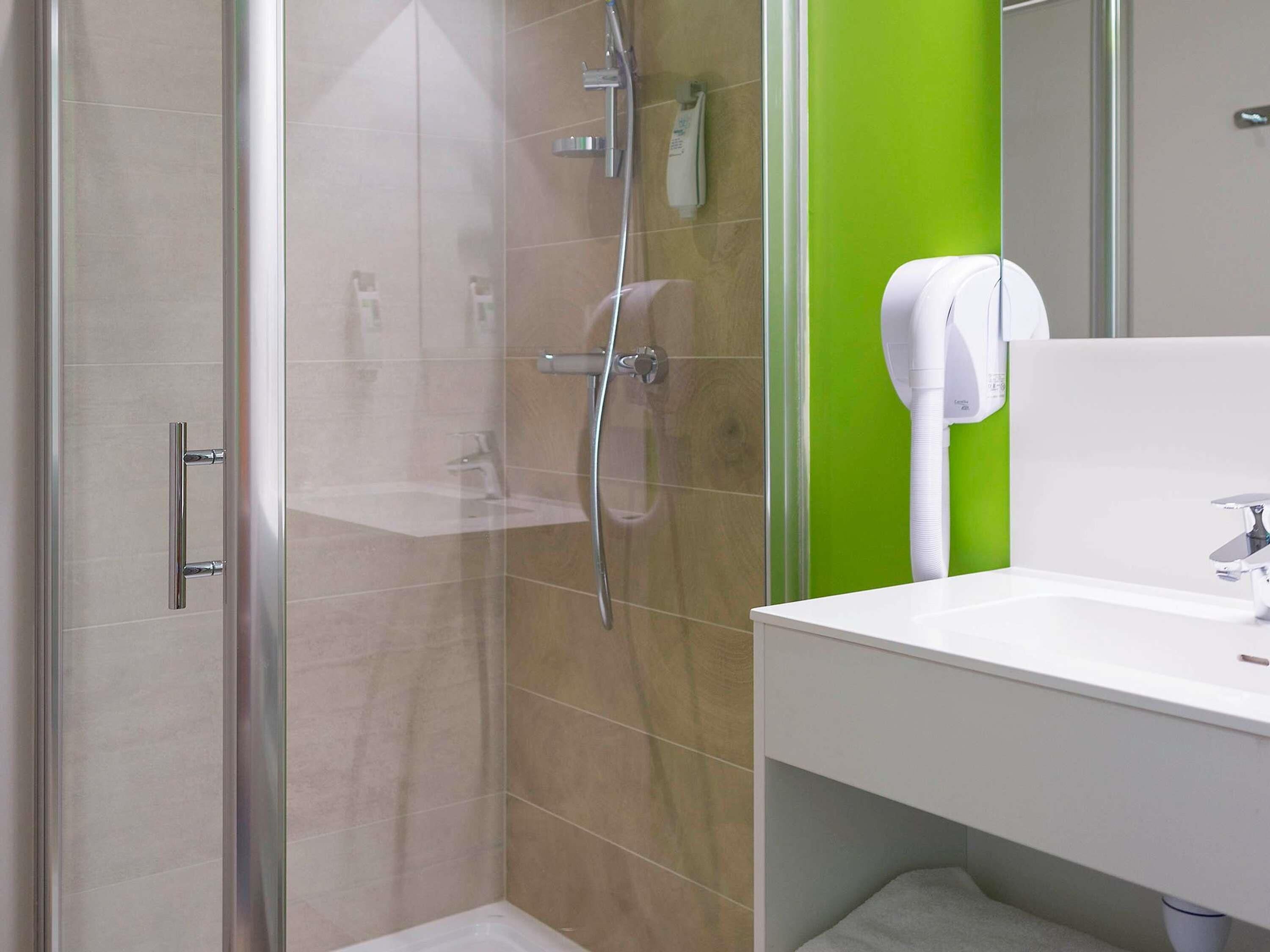 Een moderne badkamer met een douchecabine van glas, een witte wastafel en een groene accentmuur.