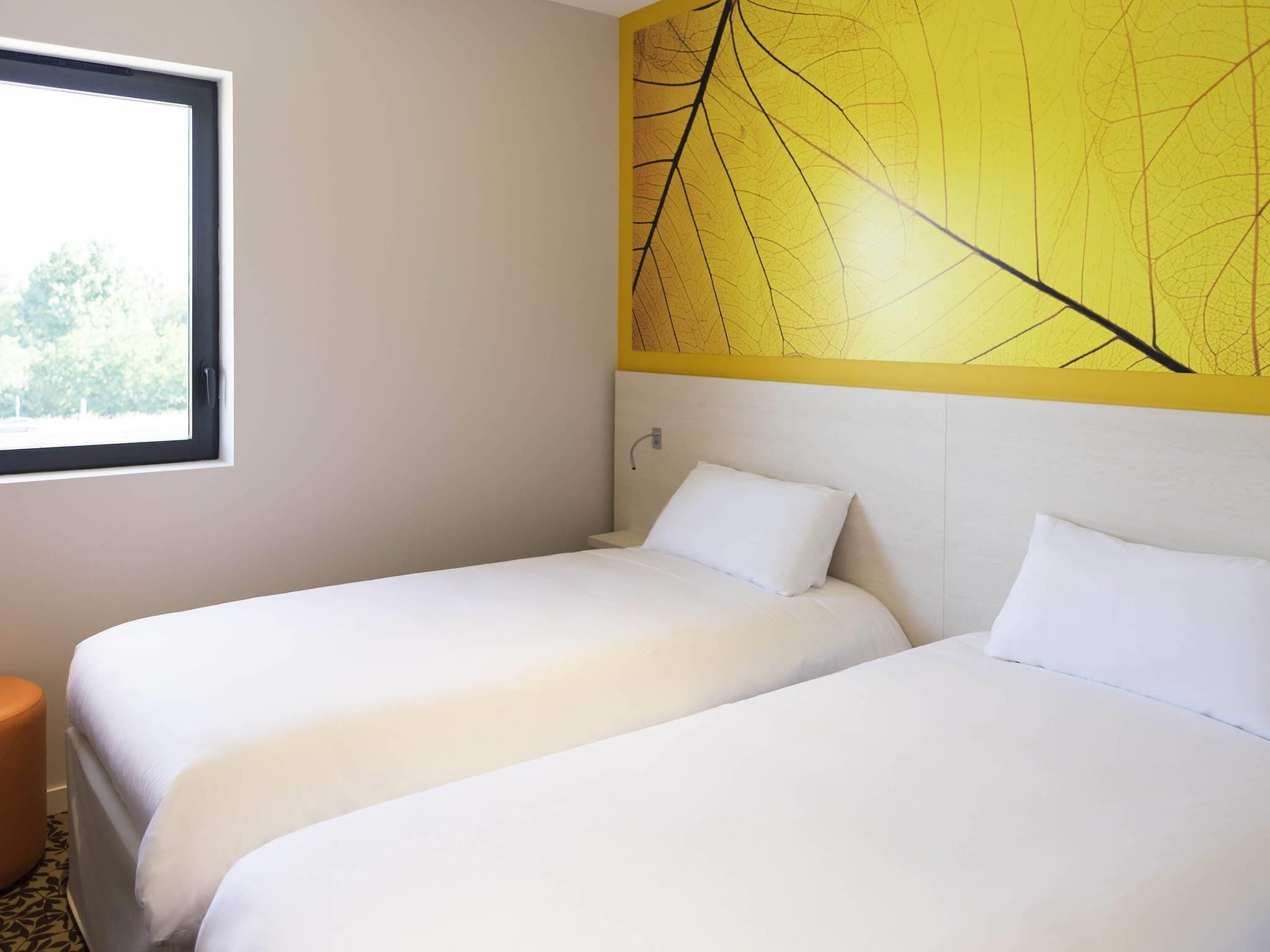 A hotel room with two beds, a window, and a yellow wall with a leaf pattern.