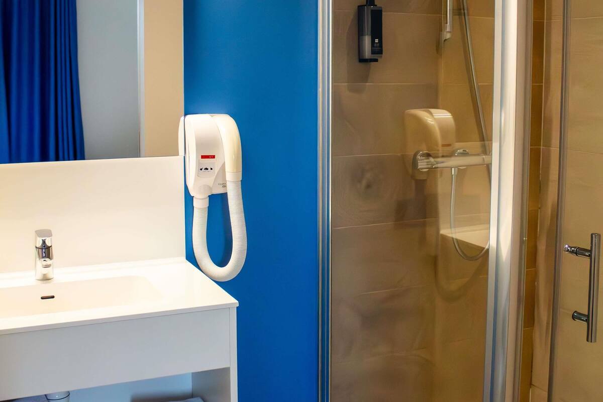 A bathroom with a white sink, a hand dryer, and a glass-enclosed shower.