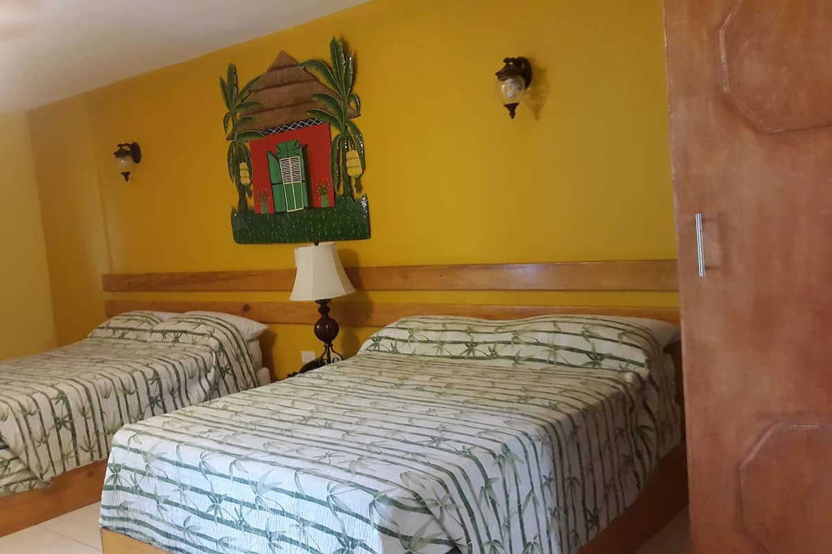 A room with two beds, a wooden headboard, a wall-mounted lamp, and a decorative wall hanging.