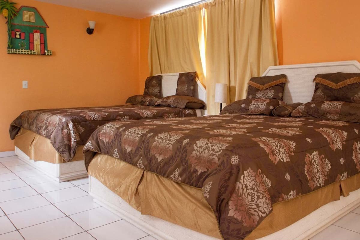 A hotel room with two beds, a nightstand, a lamp, and a wall-mounted decorative item.