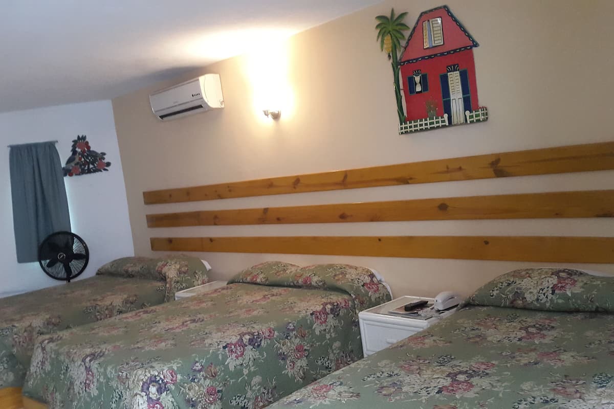 A room with a wooden headboard, floral bedding, a wall-mounted air conditioner, a small decorative house, and a fan.