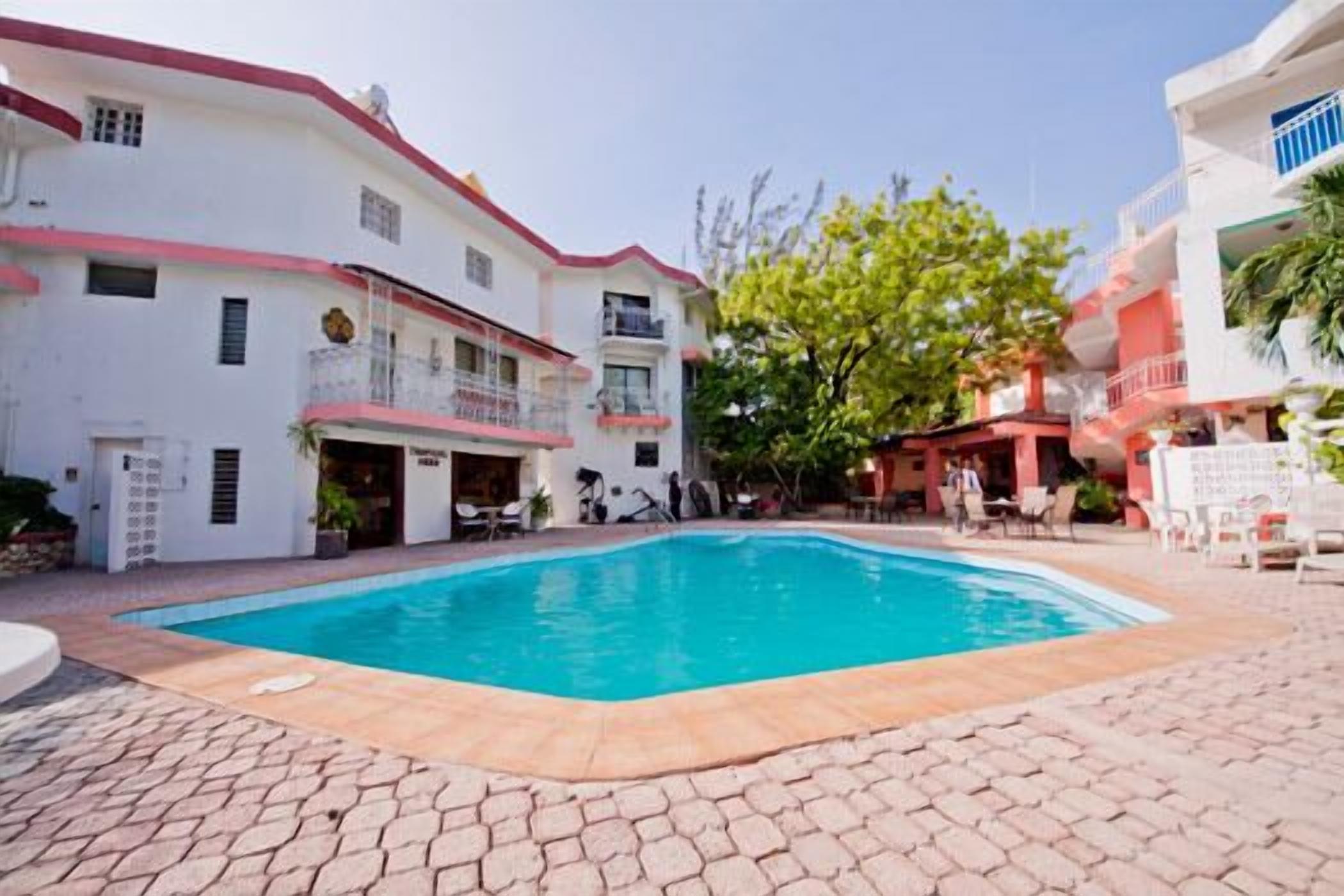 A hotel with a swimming pool, outdoor seating, and a red and white facade.